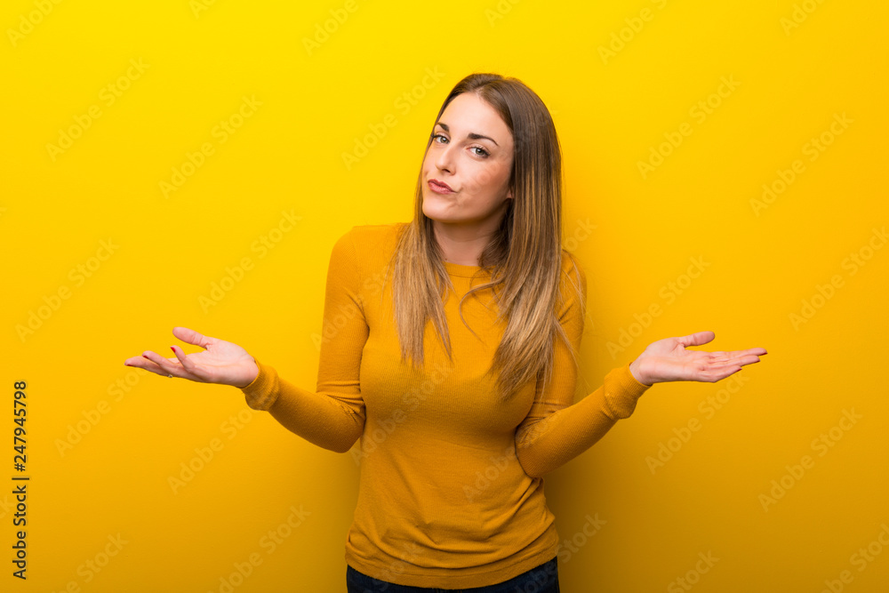 Young woman on yellow background having doubts while raising hands and shoulders Young woman on yellow background having doubts while raising hands and shoulders