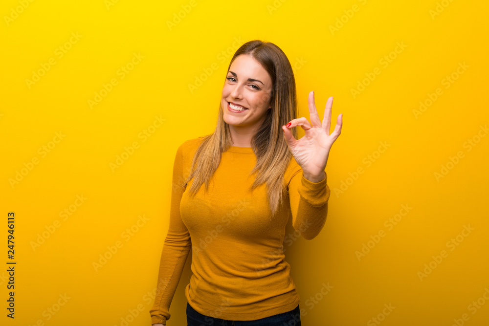 Young woman on yellow background showing an ok sign with fingers Young woman on yellow background showing an ok sign with fingers