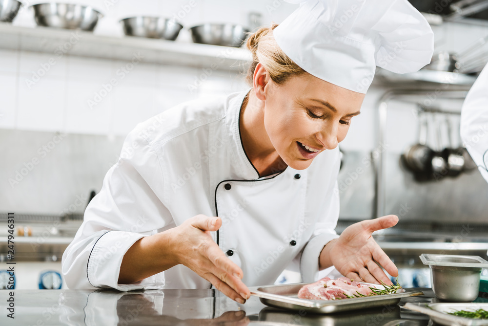 beautiful female smiling chef in uniform holding plate with meat dish in restaurant kitchen beautiful female smiling chef in uniform holding plate with meat dish in restaurant kitchen