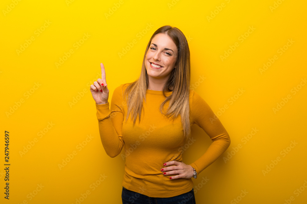 Young woman on yellow background showing and lifting a finger in sign of the best Young woman on yellow background showing and lifting a finger in sign of the best