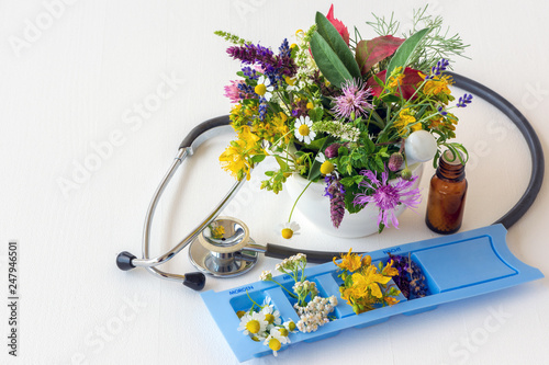 Konzept Alternativmedizin: Stethoskop mit Tablettenspender, Globuli und diversen Heilpflanzen