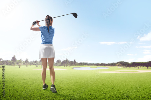 Rear view of asian woman on long drive swing with wood club in the golf course with sand bunkers, pond and trees