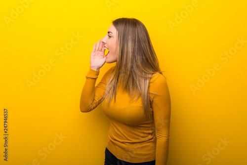 Young woman on yellow background shouting with mouth wide open to the lateral