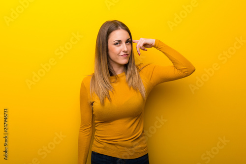 Young woman on yellow background making the gesture of madness putting finger on the head