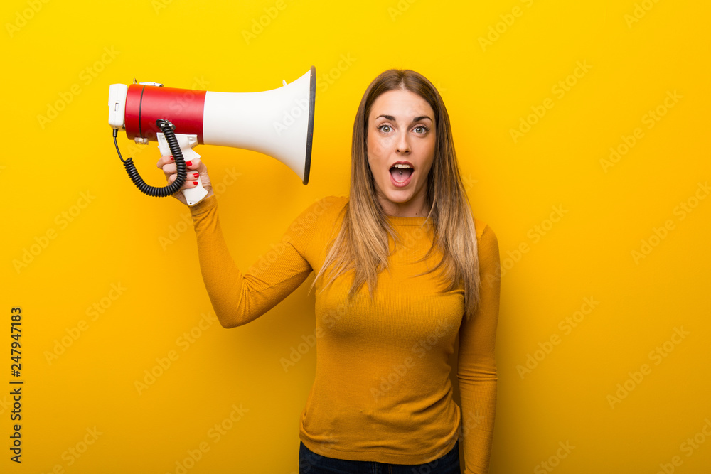 Naklejka premium Young woman on yellow background taking a megaphone that makes a lot of noise