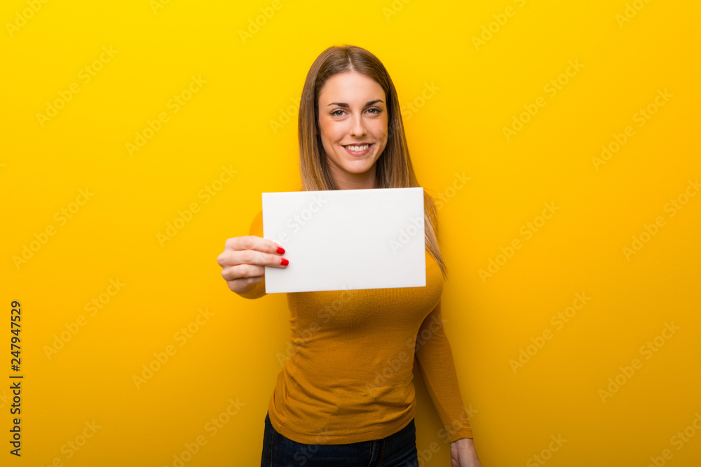 Young woman on yellow background holding an empty white placard Young woman on yellow background holding an empty white placard