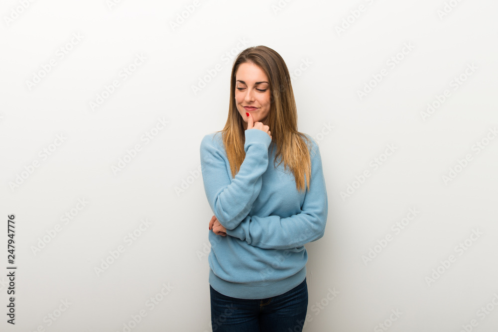 Blonde woman on isolated white background looking down with the hand on the chin Blonde woman on isolated white background looking down with the hand on the chin