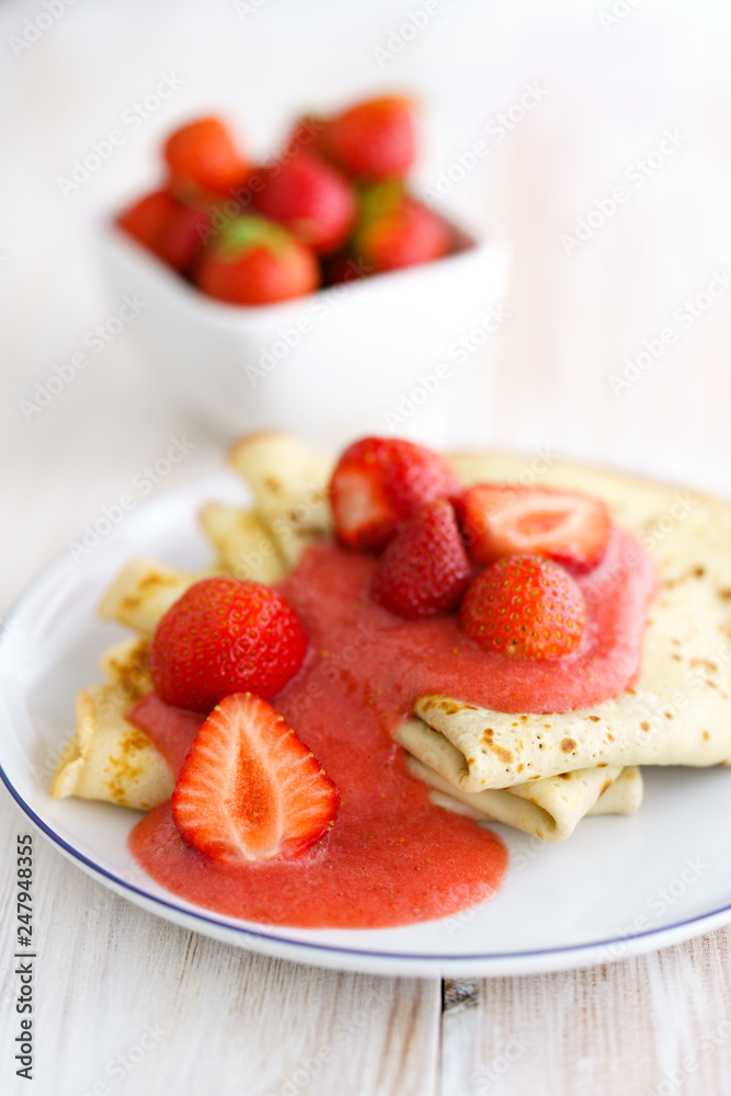 Crepes with fresh strawberries and strawberry purée on a white porcelain plate. White wooden table, high resolution Crepes with fresh strawberries and strawberry purée on a white porcelain plate. White wooden table, high resolution