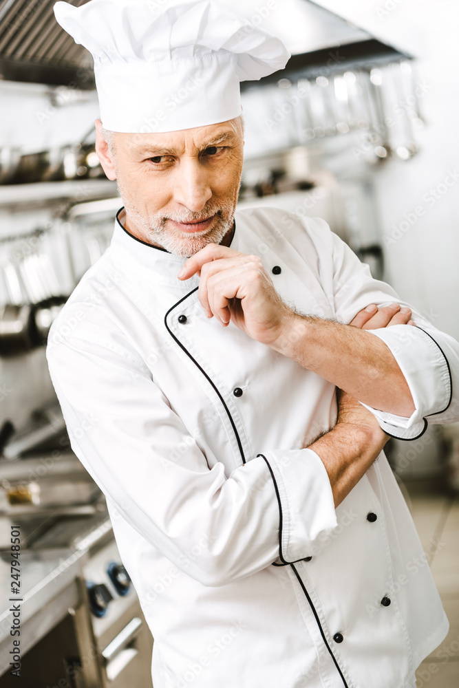 selective focus of handsome pensive male chef propping chin with hand in restaurant kitchen