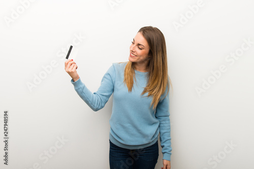 Blonde woman on isolated white background holding a credit card and thinking