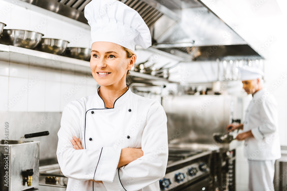 beautiful smiling female chef in uniform with arms crossed in restaurant kitchen with copy space