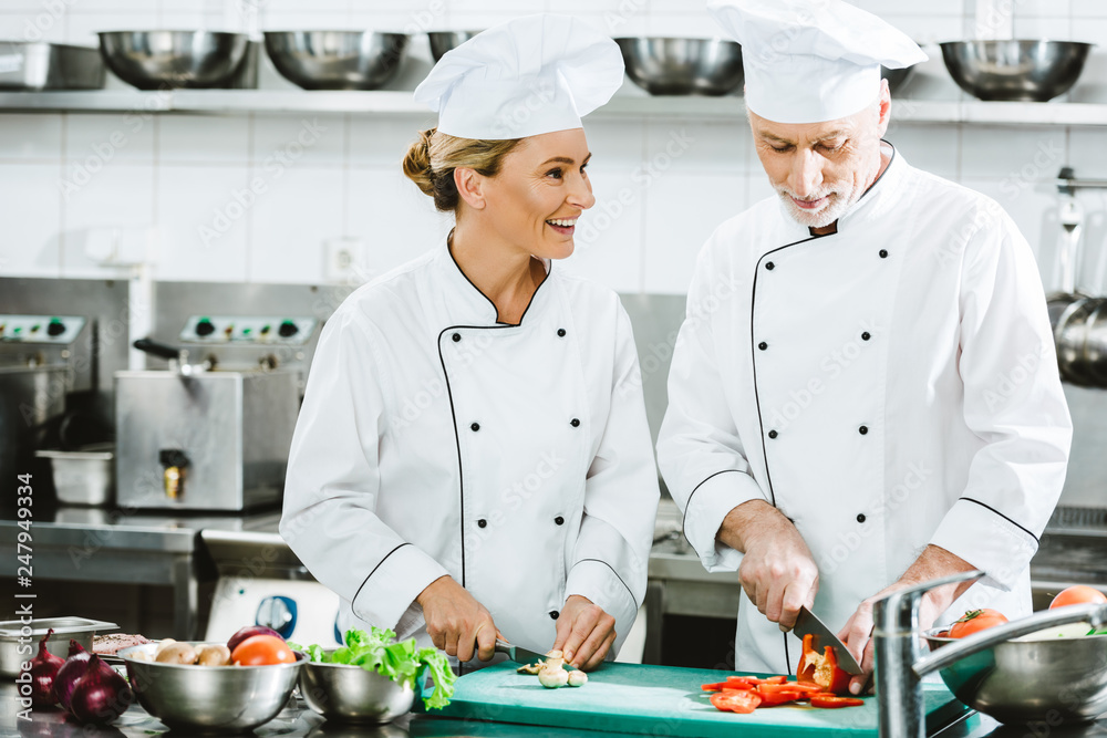 female and male chefs in uniform cutting ingredients while cooking in restaurant kitchen female and male chefs in uniform cutting ingredients while cooking in restaurant kitchen