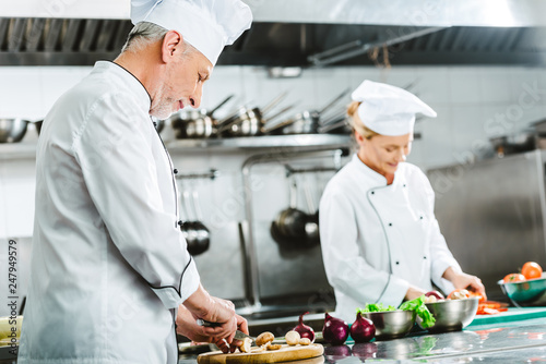 focused male and female chefs in uniform cooking in restaurant kitchen