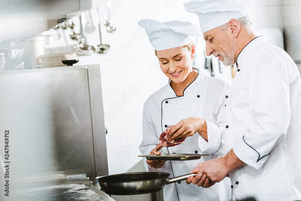 female and male chefs in uniform cooking meat on pan in restaurant kitchen with copy space female and male chefs in uniform cooking meat on pan in restaurant kitchen with copy space