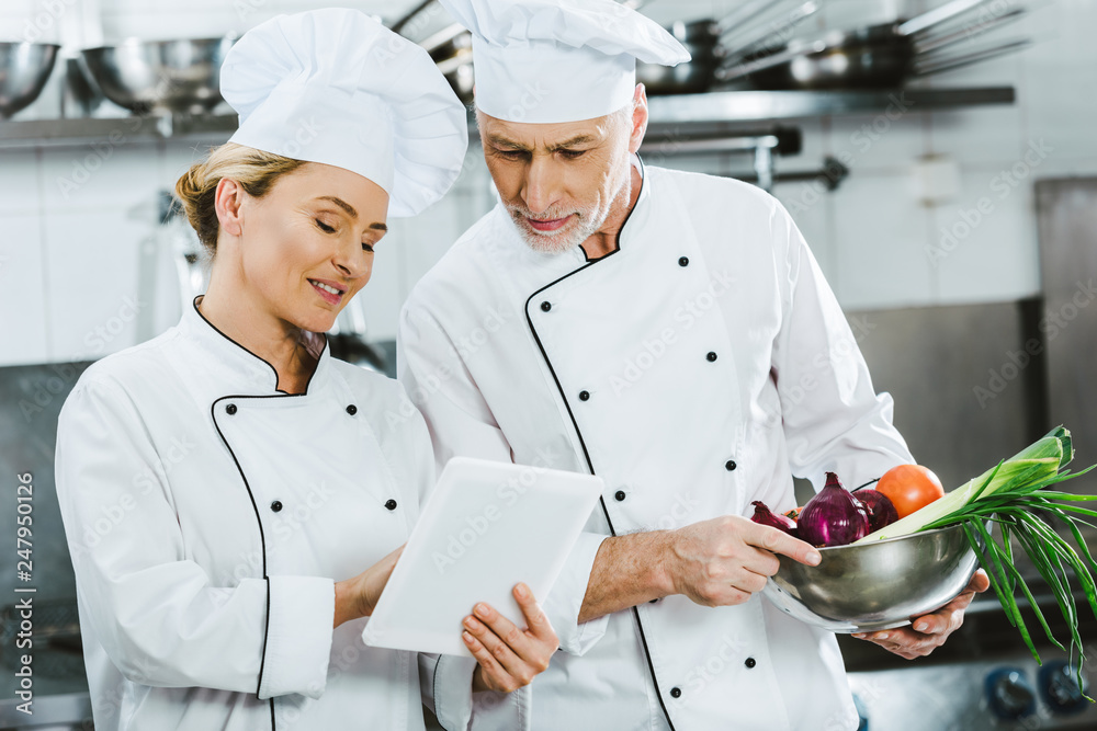 female and male chefs in uniforms using digital tablet during cooking in restaurant kitchen
