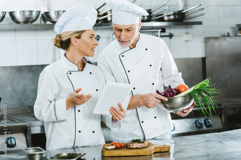female and male chefs in uniforms using digital tablet during cooking in restaurant kitchen