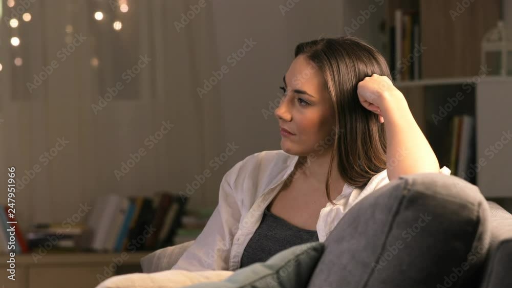 Side view portrait of a bored woman watching tv sitting on a couch at home in the night Side view portrait of a bored woman watching tv sitting on a couch at home in the night