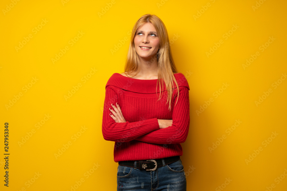 Blonde woman over yellow wall looking up while smiling Blonde woman over yellow wall looking up while smiling