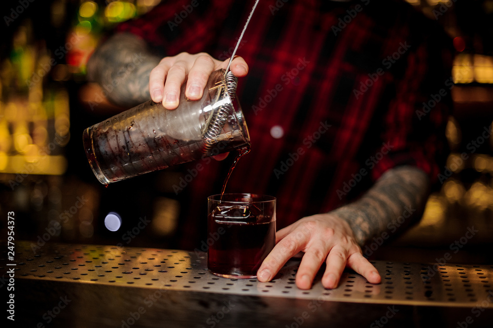 Bartender pouring fresh strong alcoholic cocktail into a glass on bar