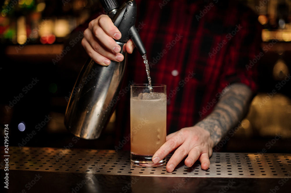 Barman adding soda water to an alcoholic orange cocktail