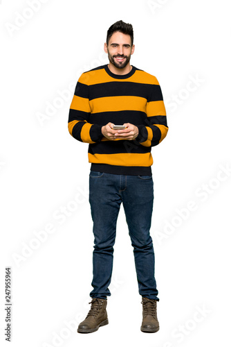 Full-length shot of Handsome man with striped sweater sending a message with the mobile on isolated white background