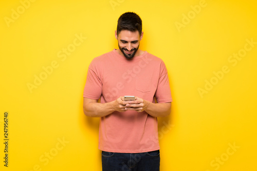 Handsome man over yellow wall sending a message with the mobile © luismolinero