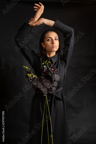 Woman wearing a black dress holding black orchid against black background