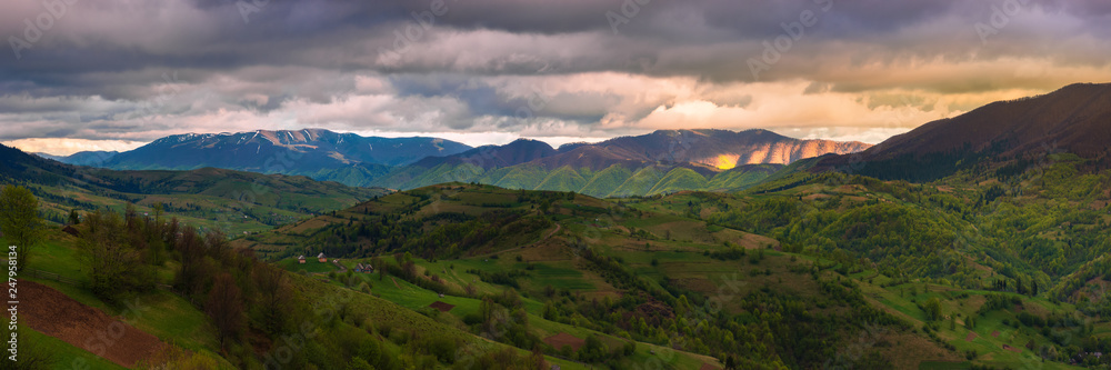panorama of a wonderful countryside in mountains. rural fields on rolling hills. village in the distant valley. beautiful landscape in spring at sunset
