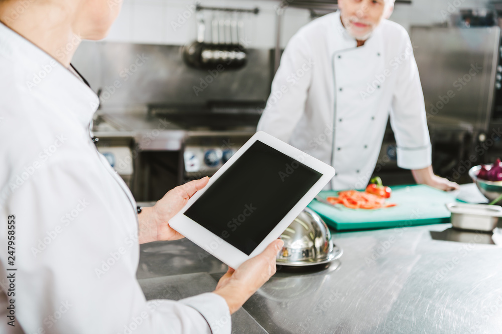 partial view of female chef using digital tablet with blank screen in restaurant kitchen partial view of female chef using digital tablet with blank screen in restaurant kitchen