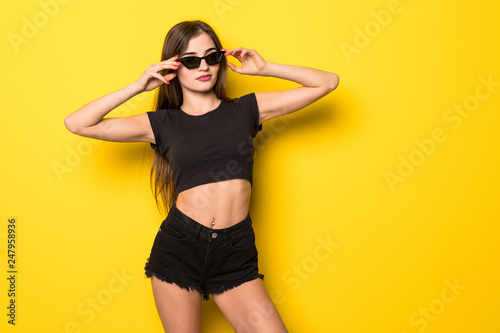 Carefree summer. Beautiful girl in summer clothes and sunglasses standing on yellow background.