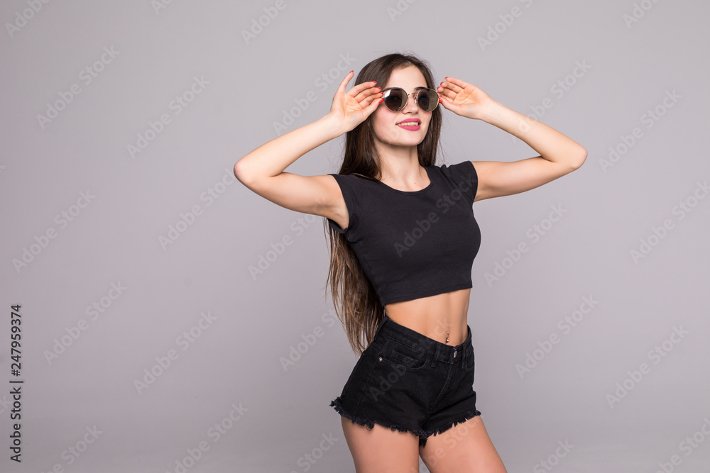 Portrait of young woman holding hands on sunglasses wearing in summer outfit isolated on gray background Portrait of young woman holding hands on sunglasses wearing in summer outfit isolated on gray background