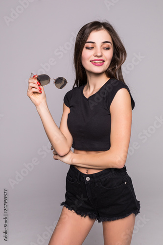 Young pretty woman in sunglasses standing posing on gray background