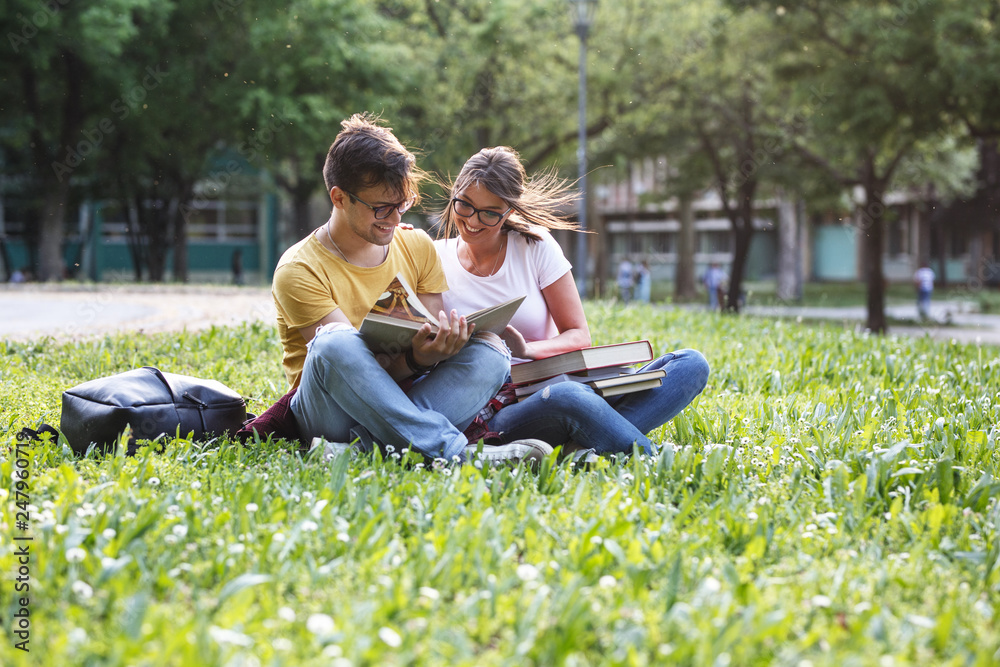 Two young students sitting at the campus yard , reading book and preparing for university exam. Two young students sitting at the campus yard , reading book and preparing for university exam.