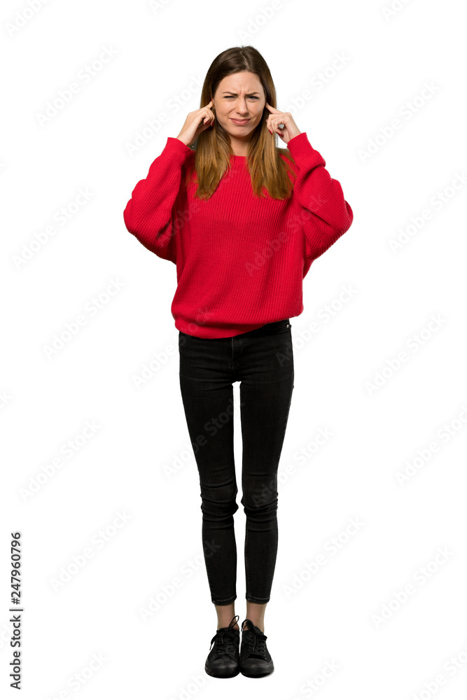 Fototapeta premium A full-length shot of a Young woman with red sweater frustrated and covering ears with hands over isolated white background