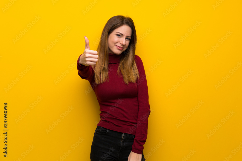Woman with turtleneck over yellow wall with thumbs up because something good has happened Woman with turtleneck over yellow wall with thumbs up because something good has happened