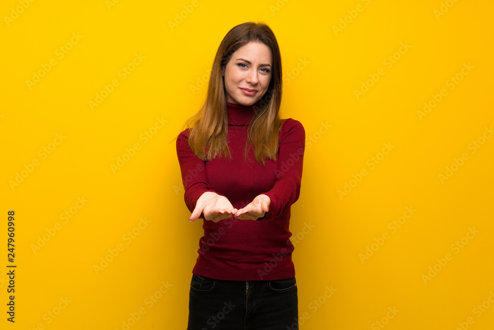Woman with turtleneck over yellow wall holding copyspace imaginary on the palm to insert an ad Woman with turtleneck over yellow wall holding copyspace imaginary on the palm to insert an ad