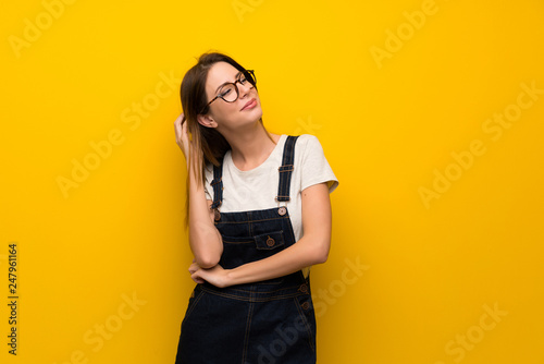 Woman over yellow wall thinking an idea while scratching head