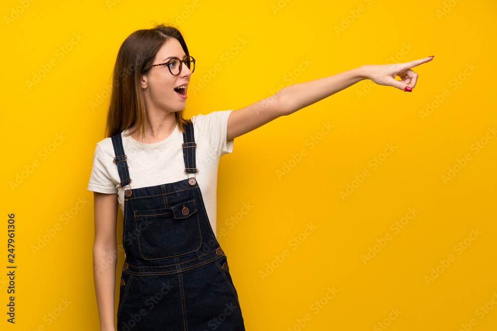 Woman over yellow wall pointing away Woman over yellow wall pointing away
