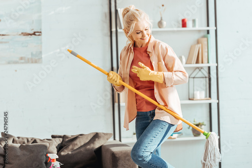 Funny senior woman playing mop guitar while cleaning house