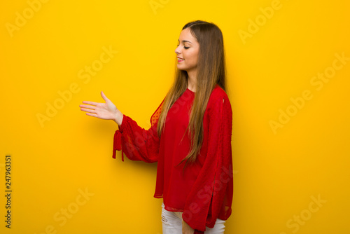 Young girl with red dress over yellow wall handshaking after good deal