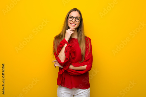 Young girl with red dress over yellow wall with glasses and smiling