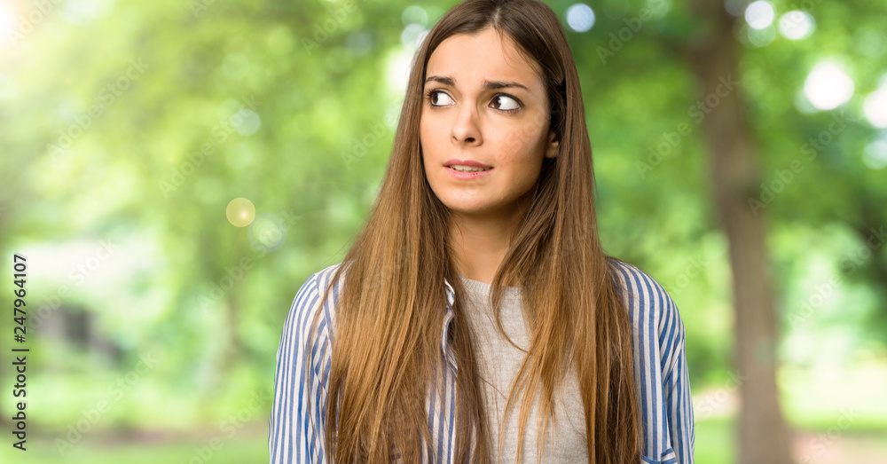 Young girl with striped shirt is a little bit nervous and scared pressing the teeth at outdoors Young girl with striped shirt is a little bit nervous and scared pressing the teeth at outdoors