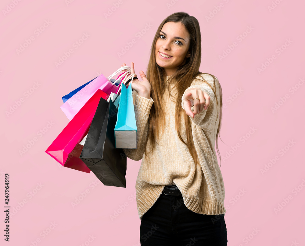 Young girl with shopping bags points finger at you with a confident expression on isolated pink background