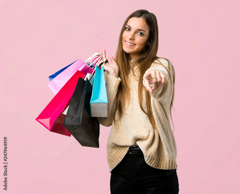 Young girl with shopping bags points finger at you with a confident expression on isolated pink background Young girl with shopping bags points finger at you with a confident expression on isolated pink background