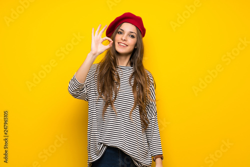 Girl with french style over yellow wall showing an ok sign with fingers photo