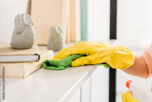 Cropped view of woman in yellow rubber glove cleaning book shelf