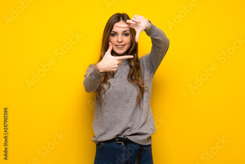 Young woman over yellow wall focusing face. Framing symbol
