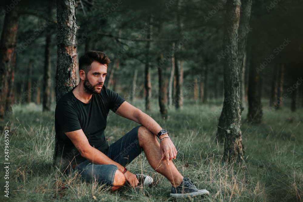 Young man sitting on grass in the woods contemplating Young man sitting on grass in the woods contemplating