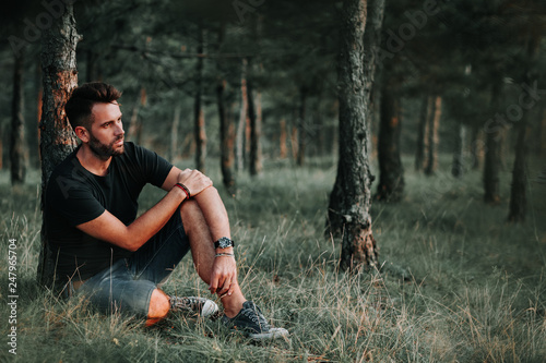 Young man sitting on grass in the woods contemplating