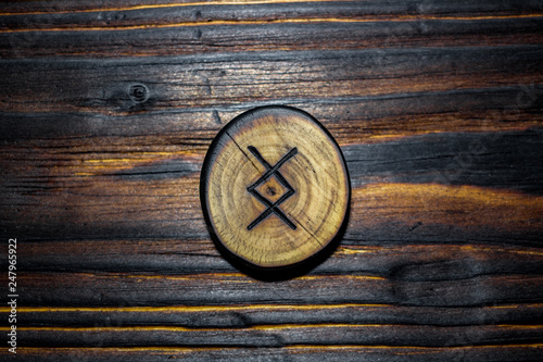 Rune Ingwaz (Yngvi) carved from wood on a wooden background - Elder Futhark photo
